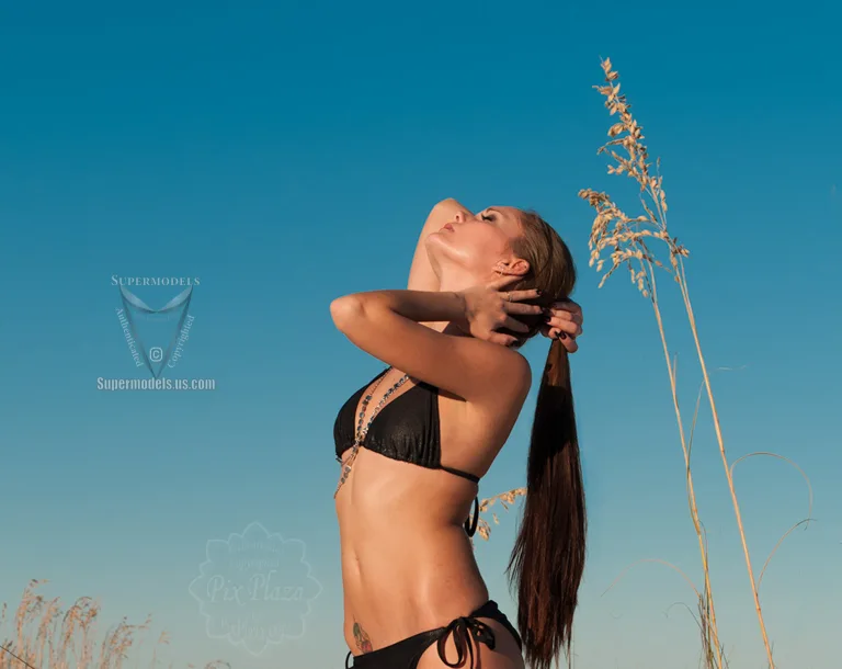 Brunette girl in black bikini on Florida beach posing with her long hair as ponytail behind her