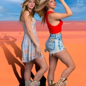 Two girls posing standing on red desert sand, looking at the camera, wearing cowgirl hats and boots