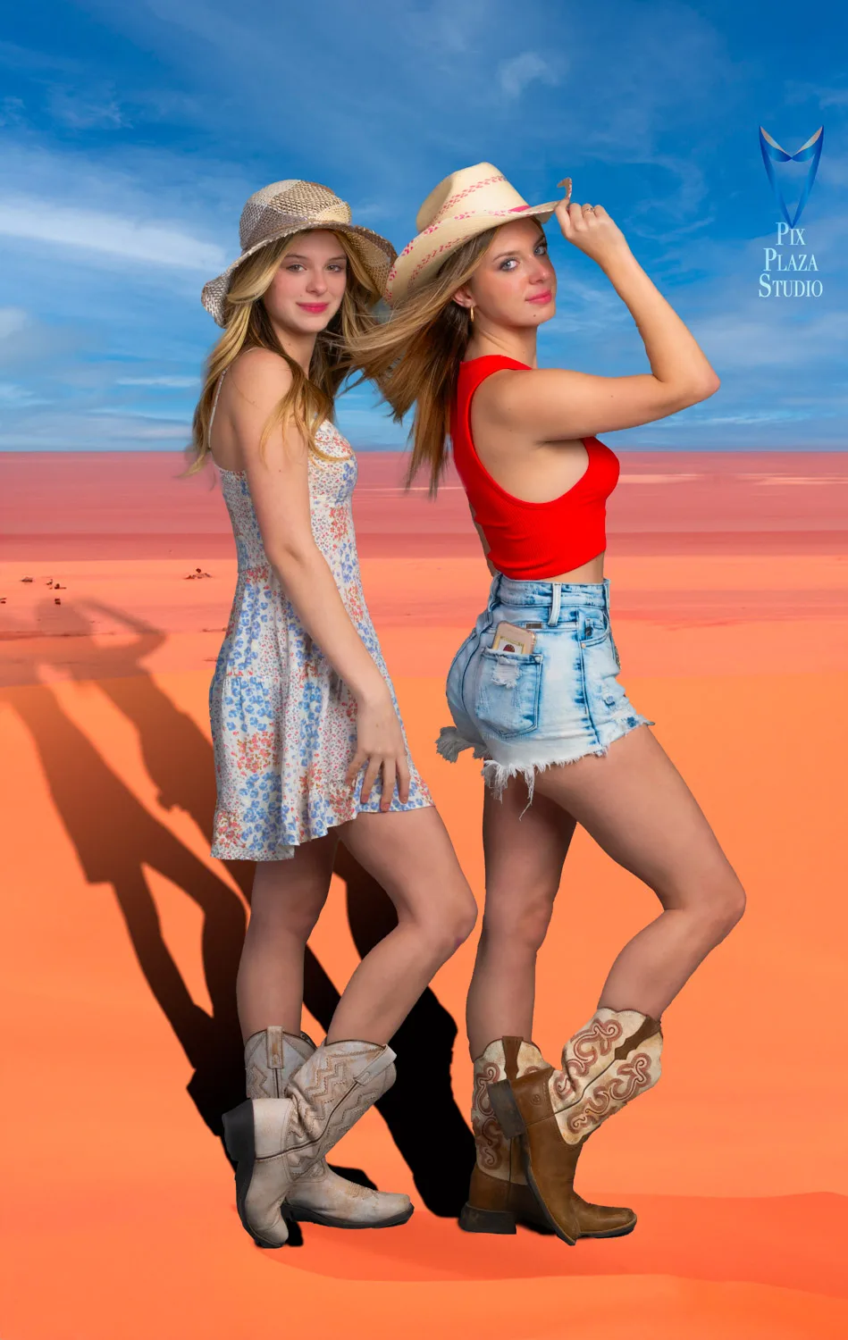 Two girls posing standing on red desert sand, looking at the camera, wearing cowgirl hats and boots