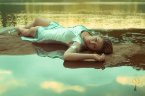 Model wearing silver dress and lying on sand island at the middle of the river