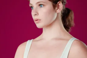 Bright blue eyed girl looking away, wearing off-white tank top in front of maroon red backdrop