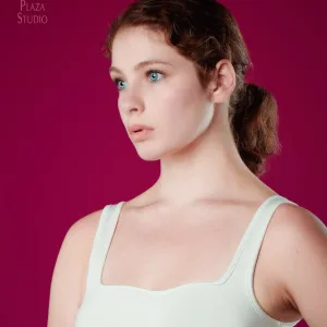Bright blue eyed girl looking away, wearing off-white tank top in front of maroon red backdrop